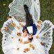 Bride and groom lying together on a lawn surrounded by autumn leaves, captured from above.