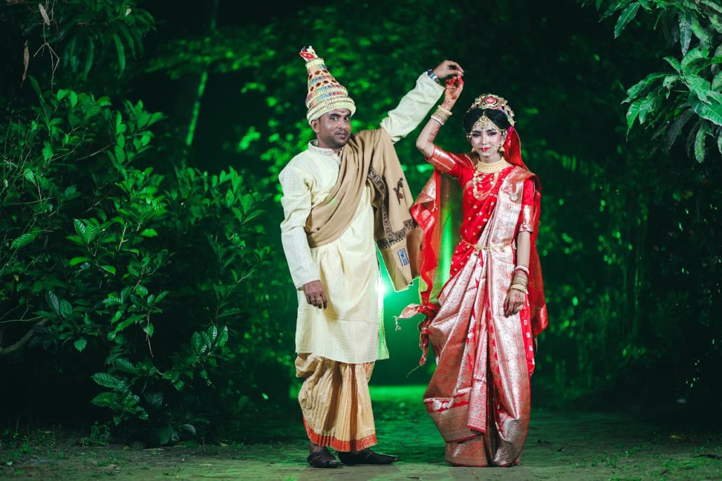 Indian couple in traditional attire celebrating their wedding outdoors amidst lush greenery.